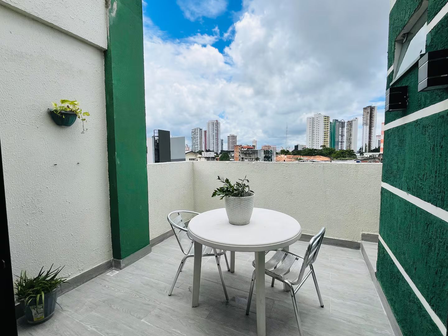 A rooftop terrace with a round table and chairs, potted plants, and a cityscape view.