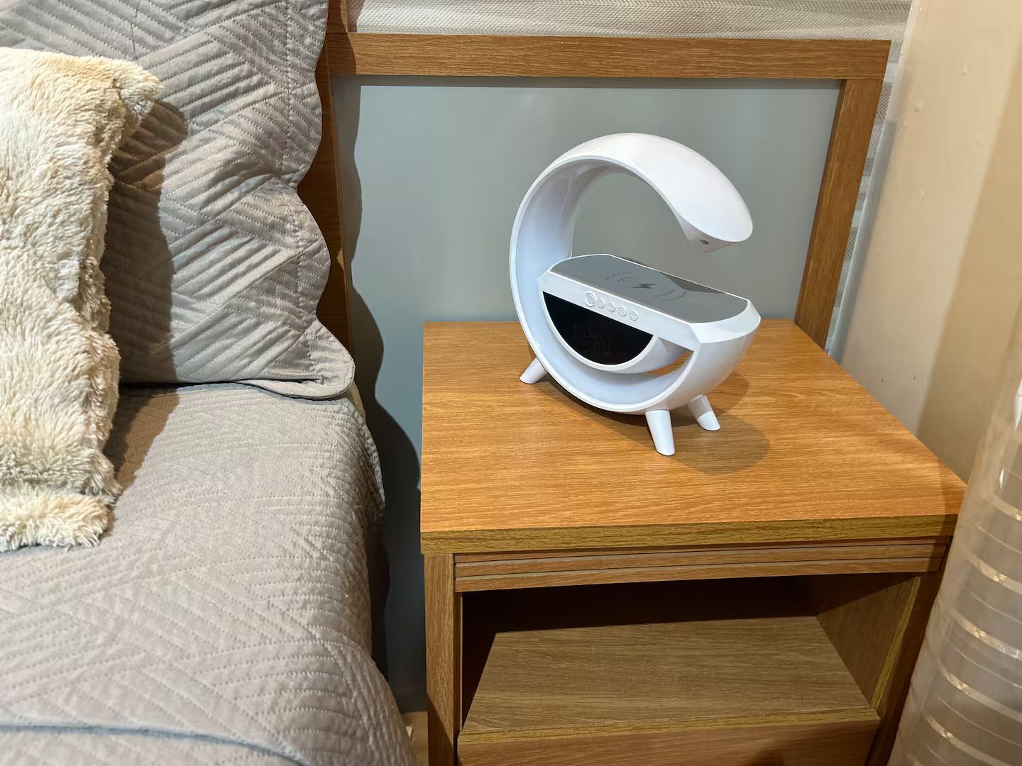 A bedside table with a white alarm clock and a wooden nightstand.
