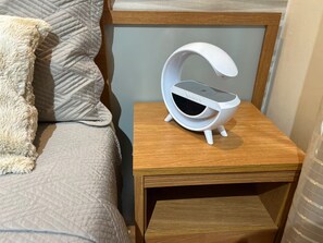 A bedside table with a white alarm clock and a wooden nightstand. - 401 Elegant and Modern Suite (Belém)