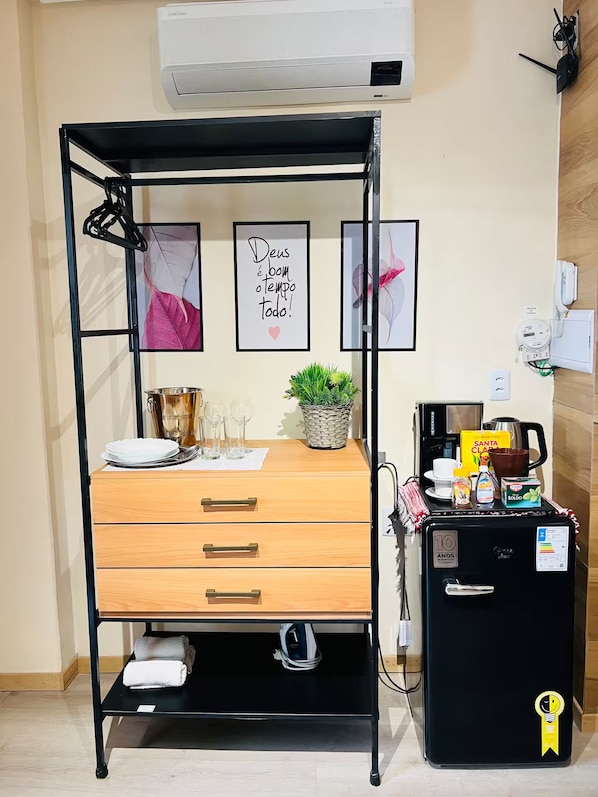 Une chambre compacte comprenant un lit, une petite table avec une plante, une machine à café et un réfrigérateur.