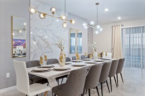 A modern dining room with a long table set for six, elegant chairs, and a chandelier with multiple light fixtures. - Themed Rooms, Game Loft, & Private Pool Near Parks (Davenport)