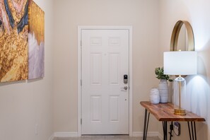 A hallway with a white door, a wooden console table with a lamp, and two vases. - Themed Rooms, Game Loft, & Private Pool Near Parks (Davenport)