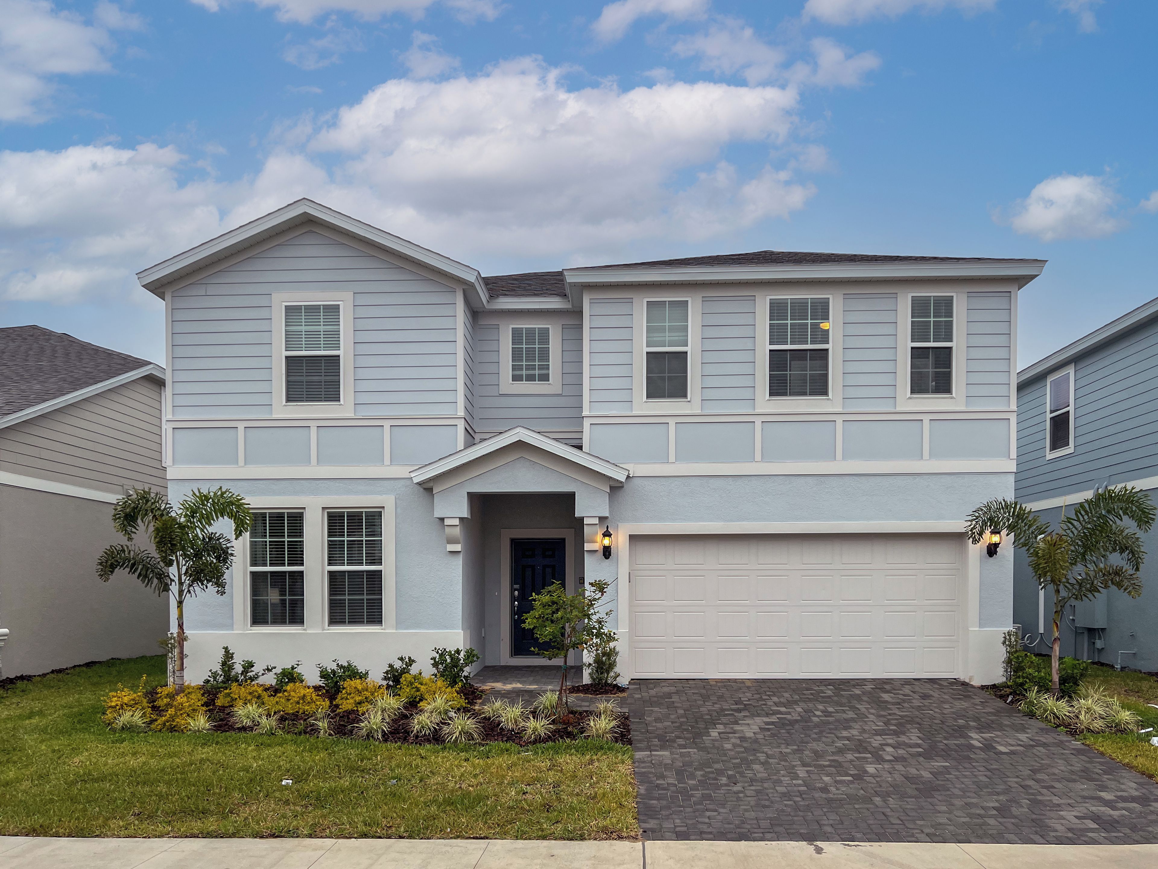 A two-story residential building with a garage, a front entrance, and a landscaped front yard.