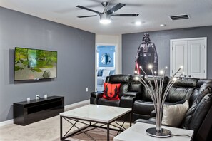 A modern living room with a flat-screen TV, a ceiling fan, a leather sofa, and a decorative Darth Vader statue. - Themed Rooms, Game Loft, & Private Pool Near Parks (Davenport)