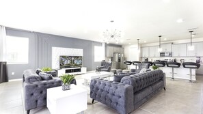A modern living room with a grey sofa, white coffee table, and a flat-screen TV. - 9BR Lake View Frozen, Batman & More (Kissimmee)