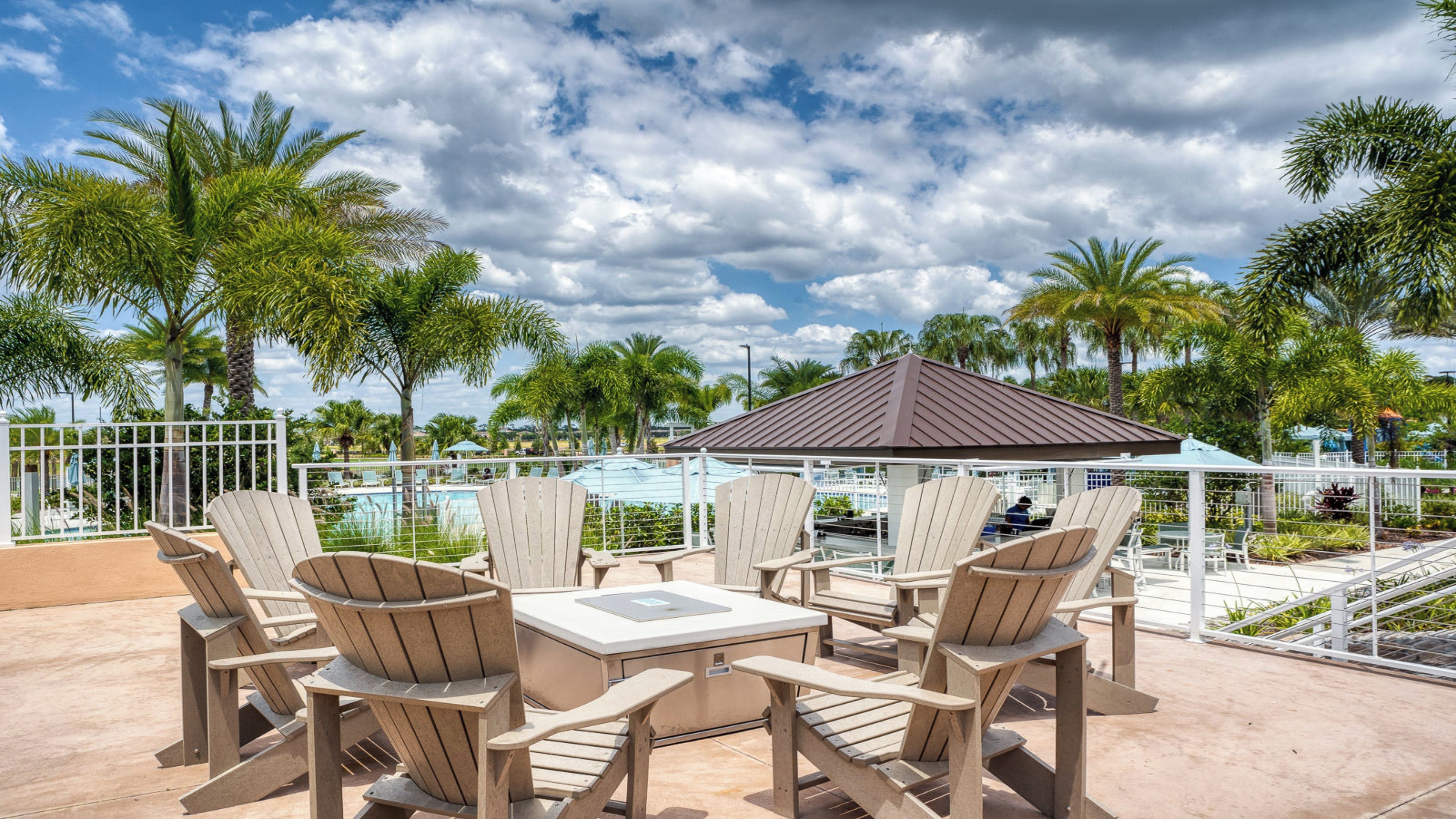 Un espace extérieur aménagé avec des chaises Adirondack et une table, offrant une vue sur une piscine et des palmiers.