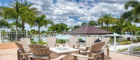 An outdoor seating area with Adirondack chairs and a table, overlooking a pool and palm trees.