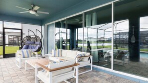 A covered outdoor seating area with a hanging chair, cushioned sofas, and a pool view. - 9BR Lake View Frozen, Batman & More (Kissimmee)
