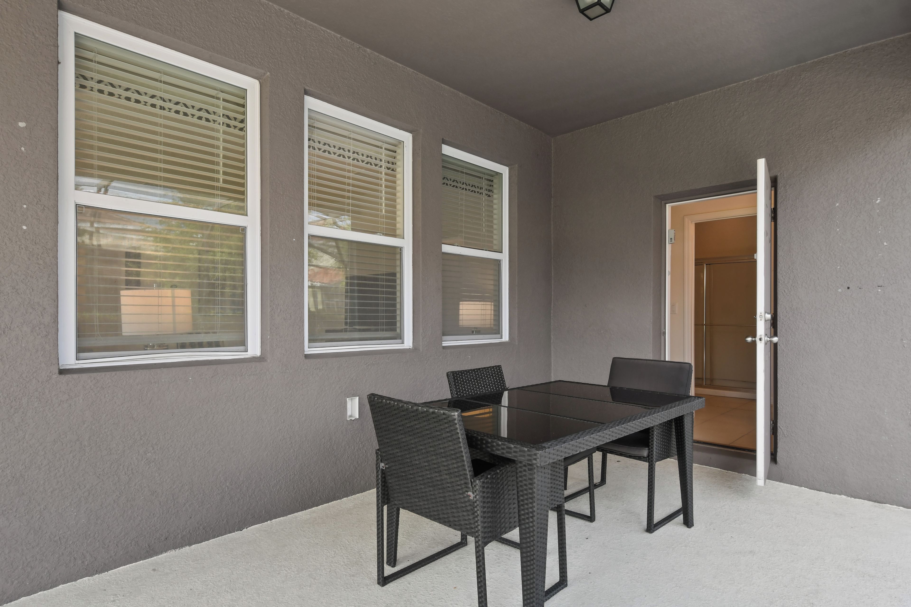 A room with a table and chairs, a door, and three windows with blinds.