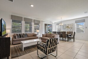 A spacious living room with a sofa, armchair, coffee table, and dining area with chairs and a table. - Game Room, Pool & Mickey-themed Retreat (Davenport)