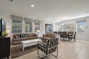 A modern living room with a sofa, armchairs, a coffee table, and a dining area with chairs and a table. - Game Room, Pool & Mickey-themed Retreat (Davenport)