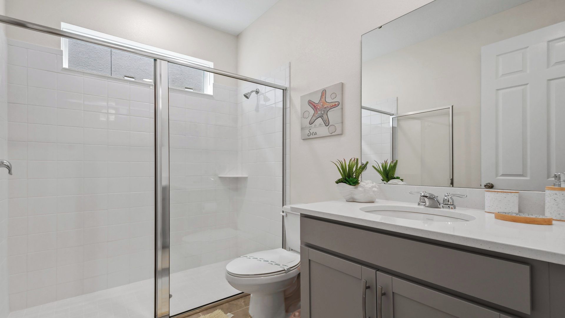 A modern bathroom with a glass shower enclosure, a white toilet, a sink with a mirror, and decorative plants.