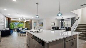 Cozinha moderna com ilha central, eletrodomésticos de aço inoxidável e iluminação pendente.