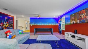 Ein Zimmer mit Billardtisch, einer Couch mit Mario-Kissen und einer Wand mit Mario Kart-Kunstwerken.