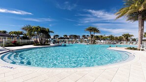 Ein großer Pool im Freien, umgeben von Palmen und Liegestühlen, mit blauem Himmel.