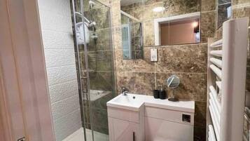 A bathroom with a glass shower enclosure, a white sink, a mirror, and a toilet.