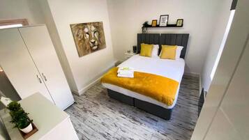A modern bedroom with a bed, a wardrobe, a painting, and a bedside table.
