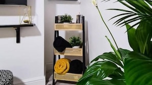 Una stanza con TV a schermo piatto, una sveglia, uno scaffale in rattan con oggetti vari e una grande pianta verde.