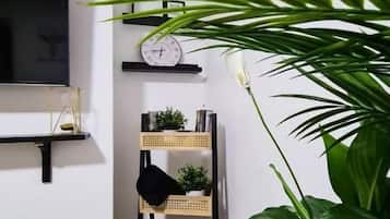 A room with a flat-screen TV, a clock, a rattan shelf with items, and a large green plant.
