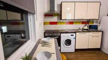 A compact kitchen with a washing machine, a microwave, and a window.