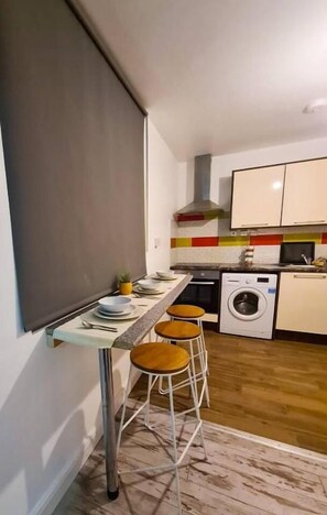 A compact kitchen with a bar area, a washing machine, and a tiled backsplash. - Modern 1 Bedroom flat in City center (Leicester)