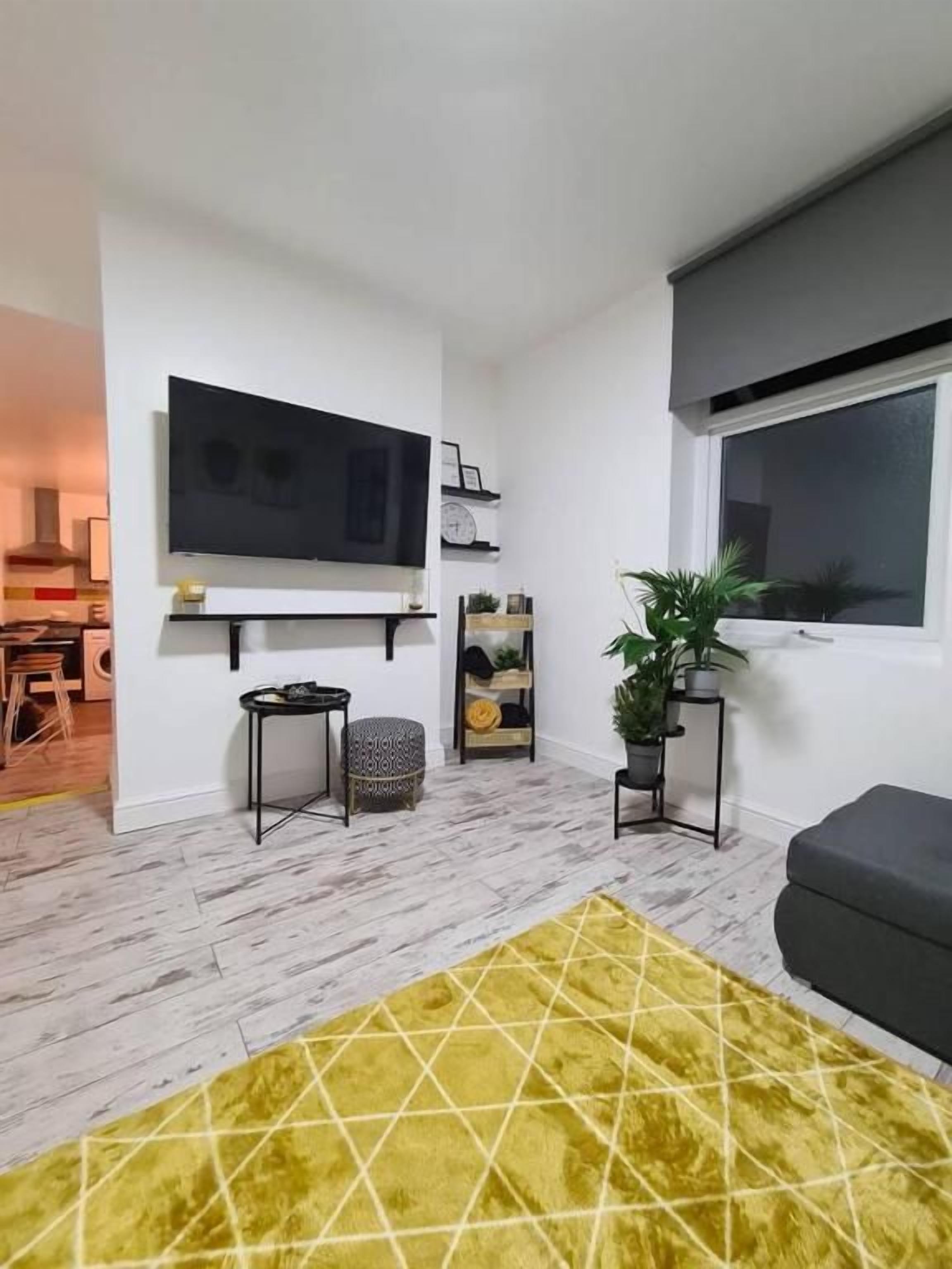 A modern living room with a flat-screen TV mounted on the wall, a sofa, a coffee table, and a yellow rug.