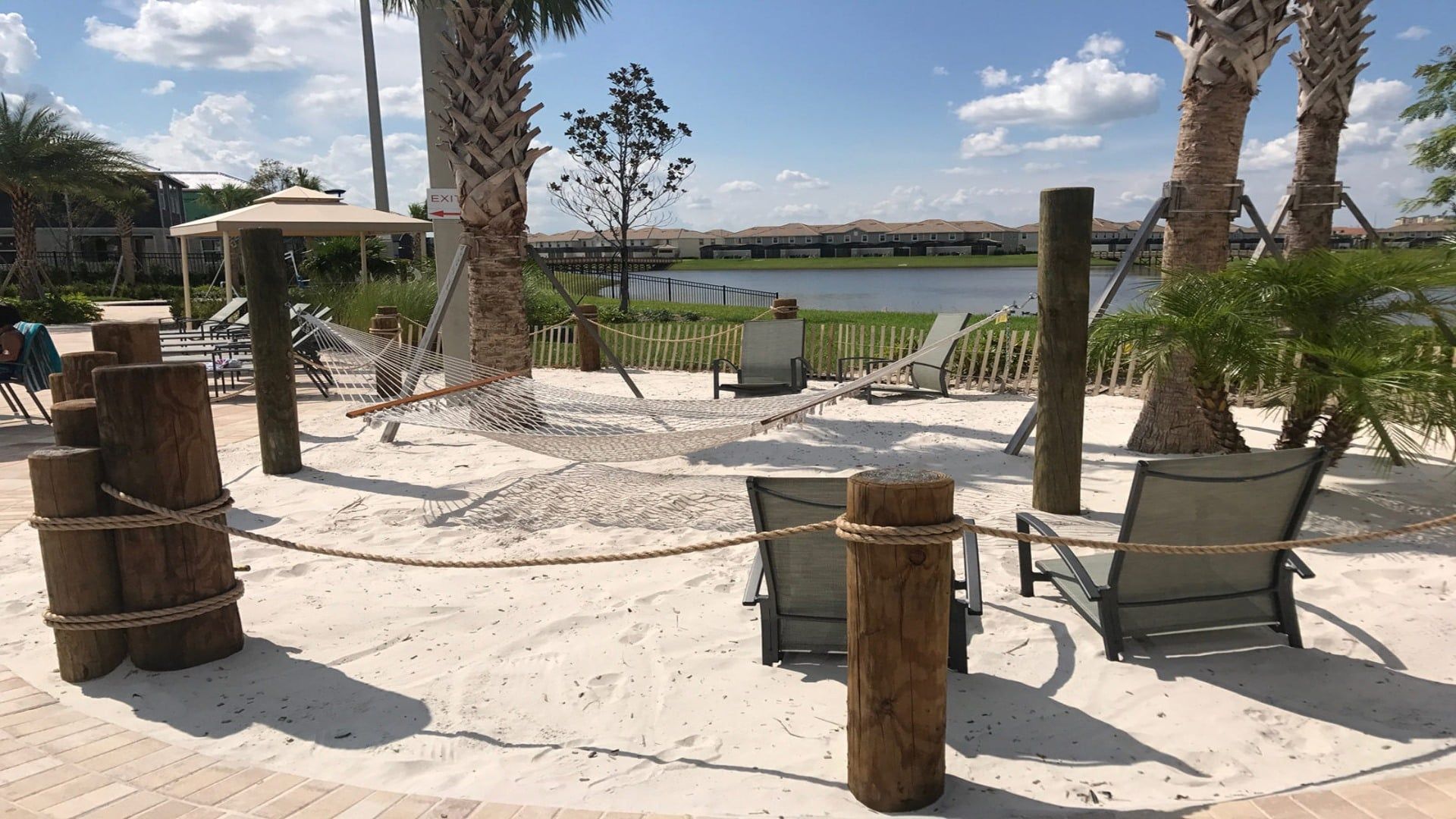 A sandy outdoor area with a hammock, chairs, and a view of a body of water.