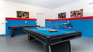 Ein Billardtisch in einem Raum mit blauen und roten Wänden, zwei gerahmte Bilder an der Wand und eine Tür.