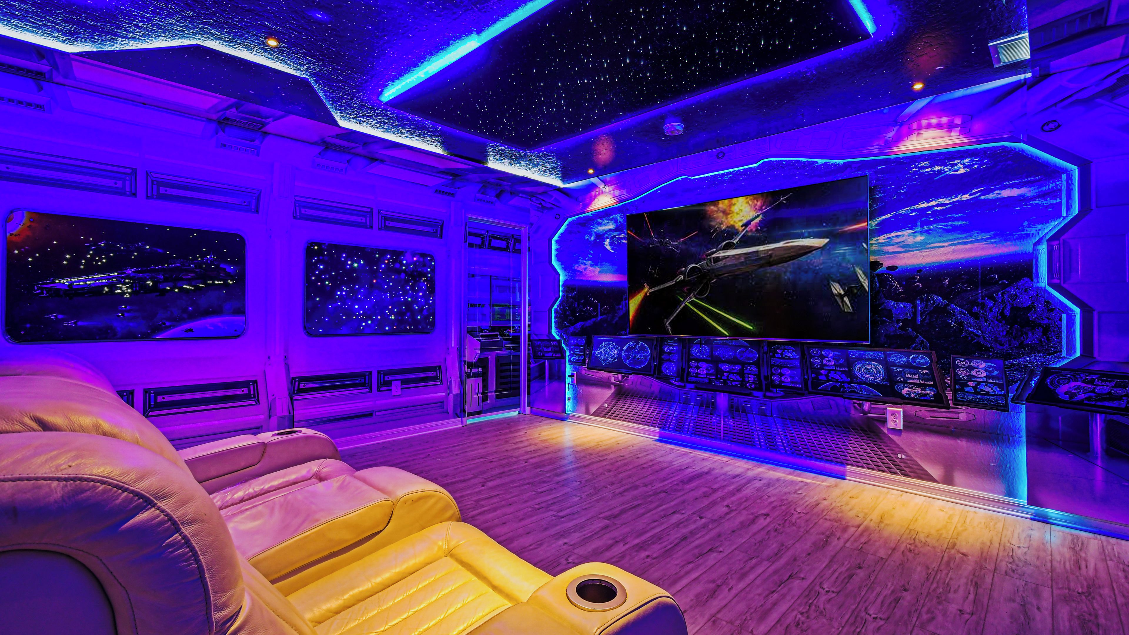 A room with a large screen displaying a space-themed image, a control panel, and a reclining chair.