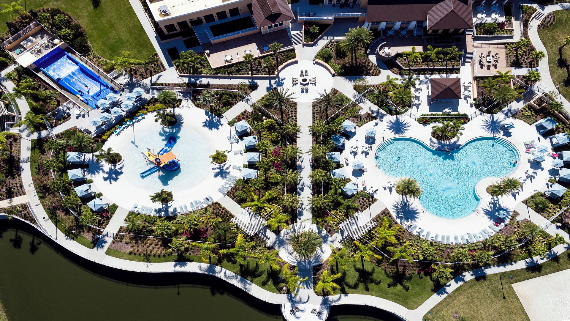 An aerial view of a resort with a central pool area, multiple smaller pools, and a variety of outdoor seating arrangements.