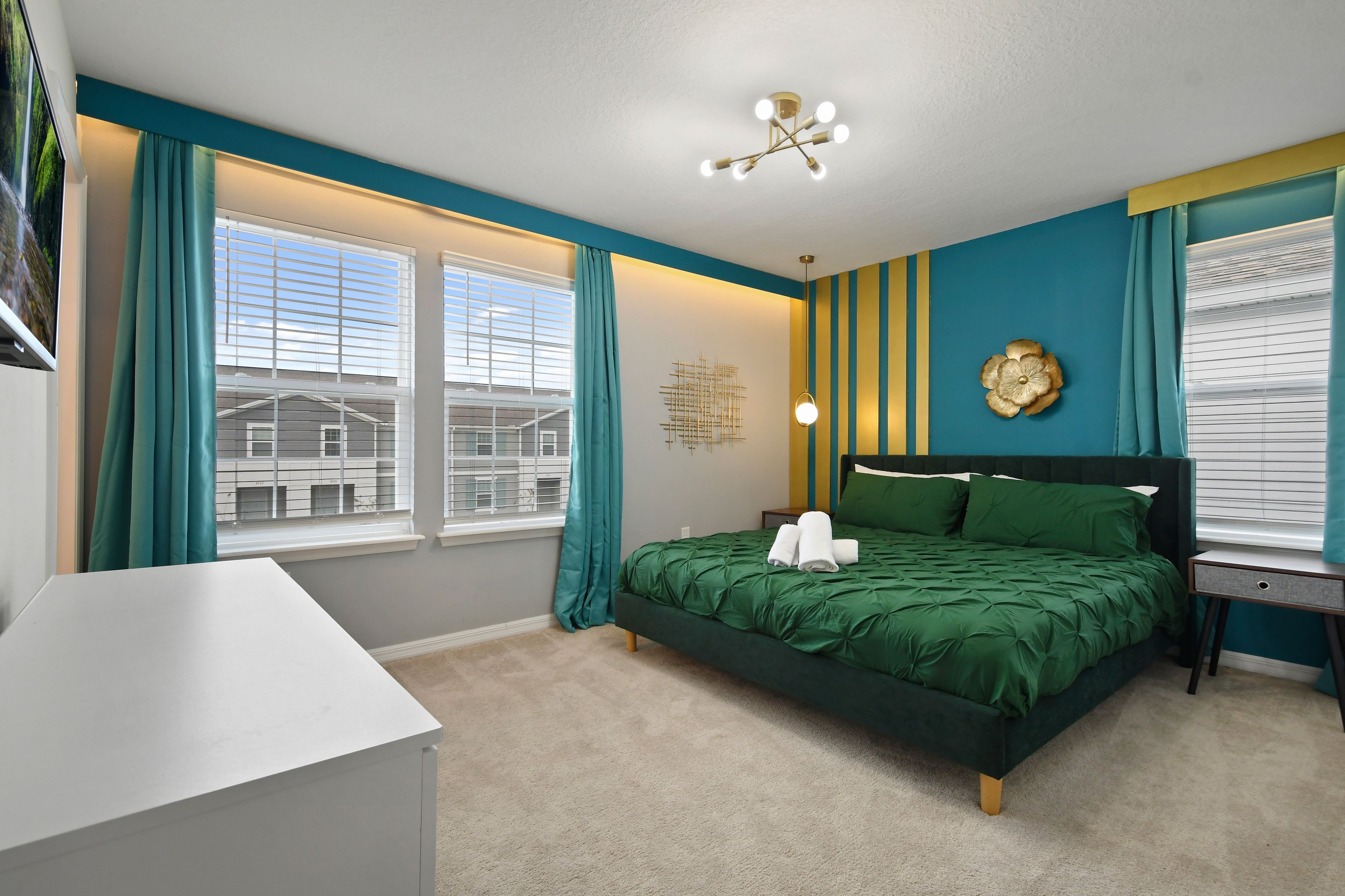 A bedroom with a bed, a bedside table, a window with curtains, a wall clock, and a ceiling light fixture.