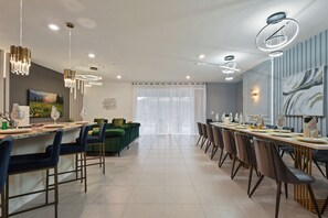 A modern dining area with a long table set for a meal, a green sofa, and a painting on the wall. - Luxury Villa w/ Pool, Spa & Star Wars Theater (Davenport)