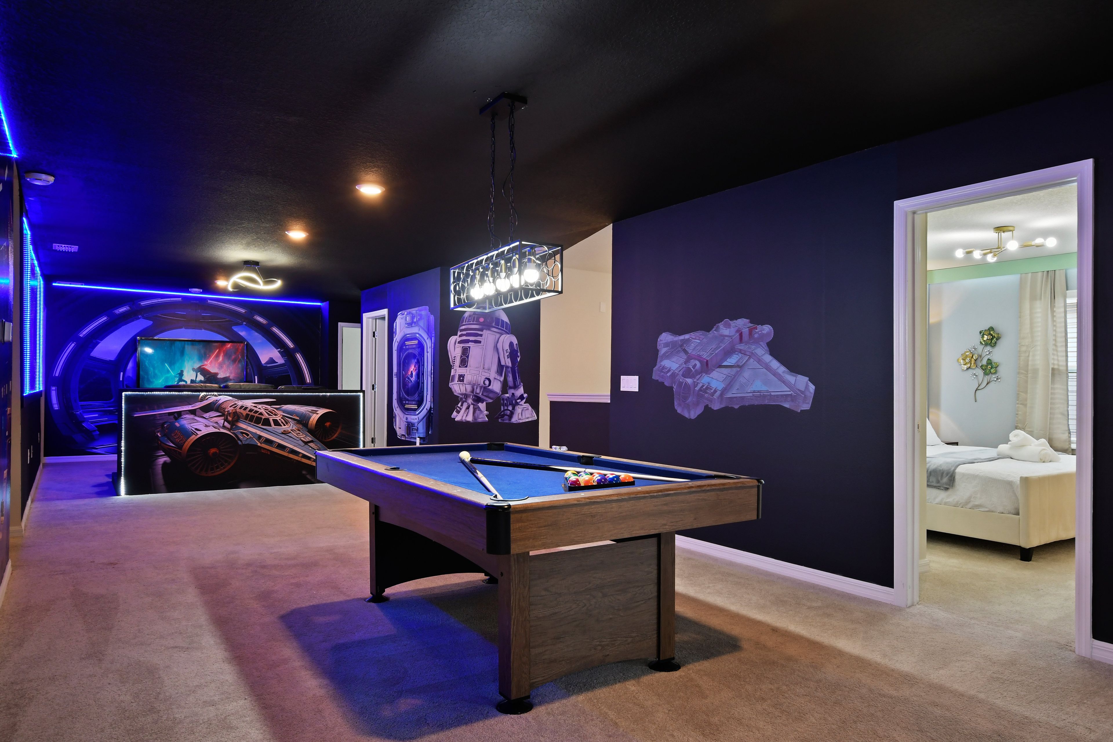A pool table in a room with dark walls, a ceiling light, and Star Wars-themed decorations.