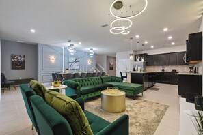 A modern living room with a green sectional sofa, a round coffee table, and a dining area with a high table and chairs. - Luxury Villa w/ Pool, Spa & Star Wars Theater (Davenport)