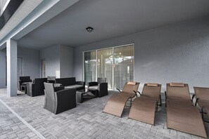 A covered outdoor seating area with wicker furniture and sun loungers, a glass door entrance, and a tiled floor. - Luxury Villa w/ Pool, Spa & Star Wars Theater (Davenport)