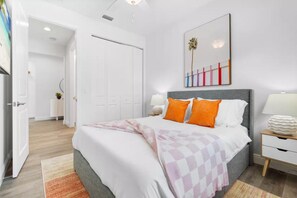 A modern bedroom with a large bed, a bedside table with a lamp, and a door leading to another room. - Near "The Ave" sleeps 10 Discounted Nights (Delray Beach)