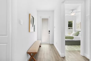 Ein Flur mit einer Bank, einer Tür und einem Schlafzimmer mit Bett und Deckenventilator.