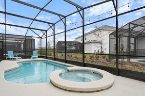 Une piscine intérieure avec un jacuzzi, entourée d’une structure en verre abritant des chaises et offrant une vue sur les maisons.