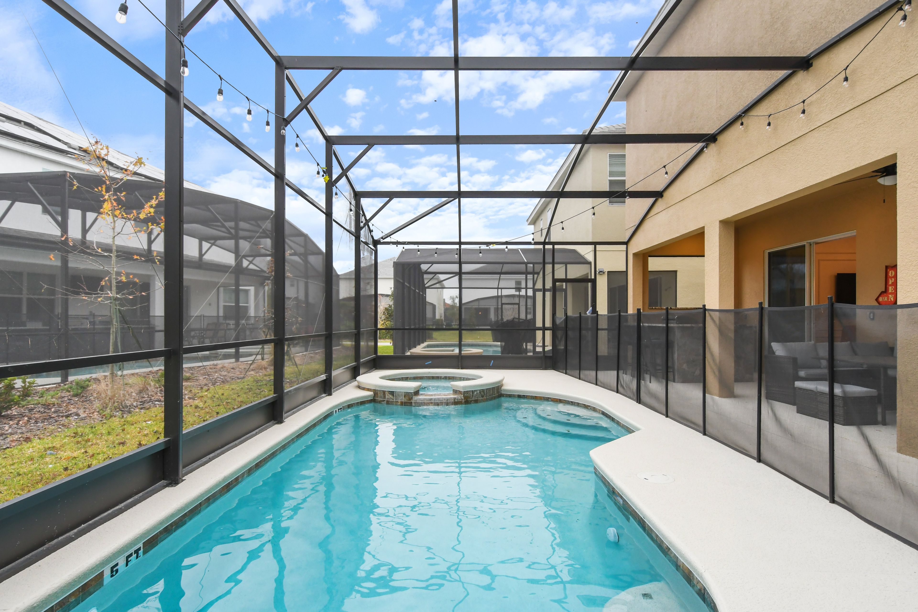 A swimming pool with a glass enclosure, a hot tub, and a covered patio area.