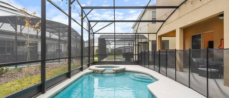 A swimming pool with a glass enclosure, a hot tub, and a covered patio area.