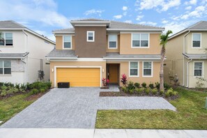A two-story residential building with a garage, a driveway, and a well-maintained garden. - Discounted 12br w Barbie Castle/dino Slide/games (Kissimmee)