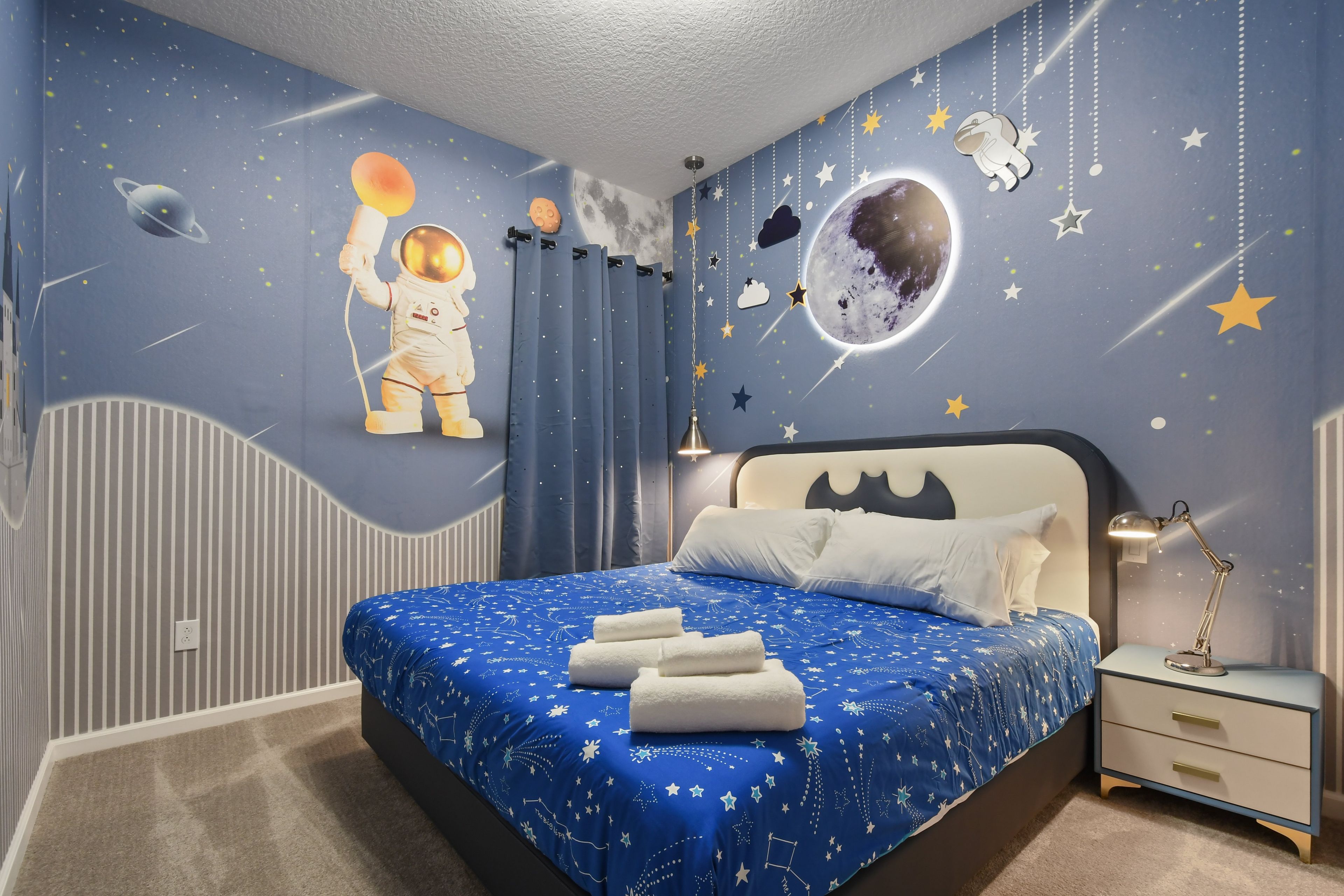 A bedroom with a bed, nightstand, and wall decorations including a space-themed mural.