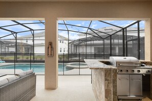 An outdoor kitchen area with a grill, a pool, and a seating area. - Discounted 12br w Barbie Castle/dino Slide/games (Kissimmee)