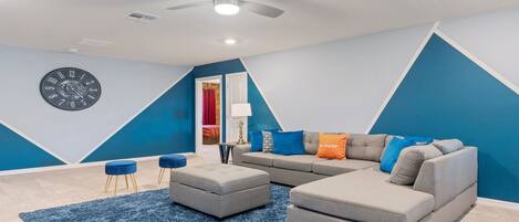 A modern living room with a sectional sofa, ottoman, and blue accent pillows.