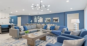 Ein modernes Wohnzimmer mit einem Ecksofa, einem Couchtisch und einem Essbereich, im Hintergrund ist eine Küche zu sehen.