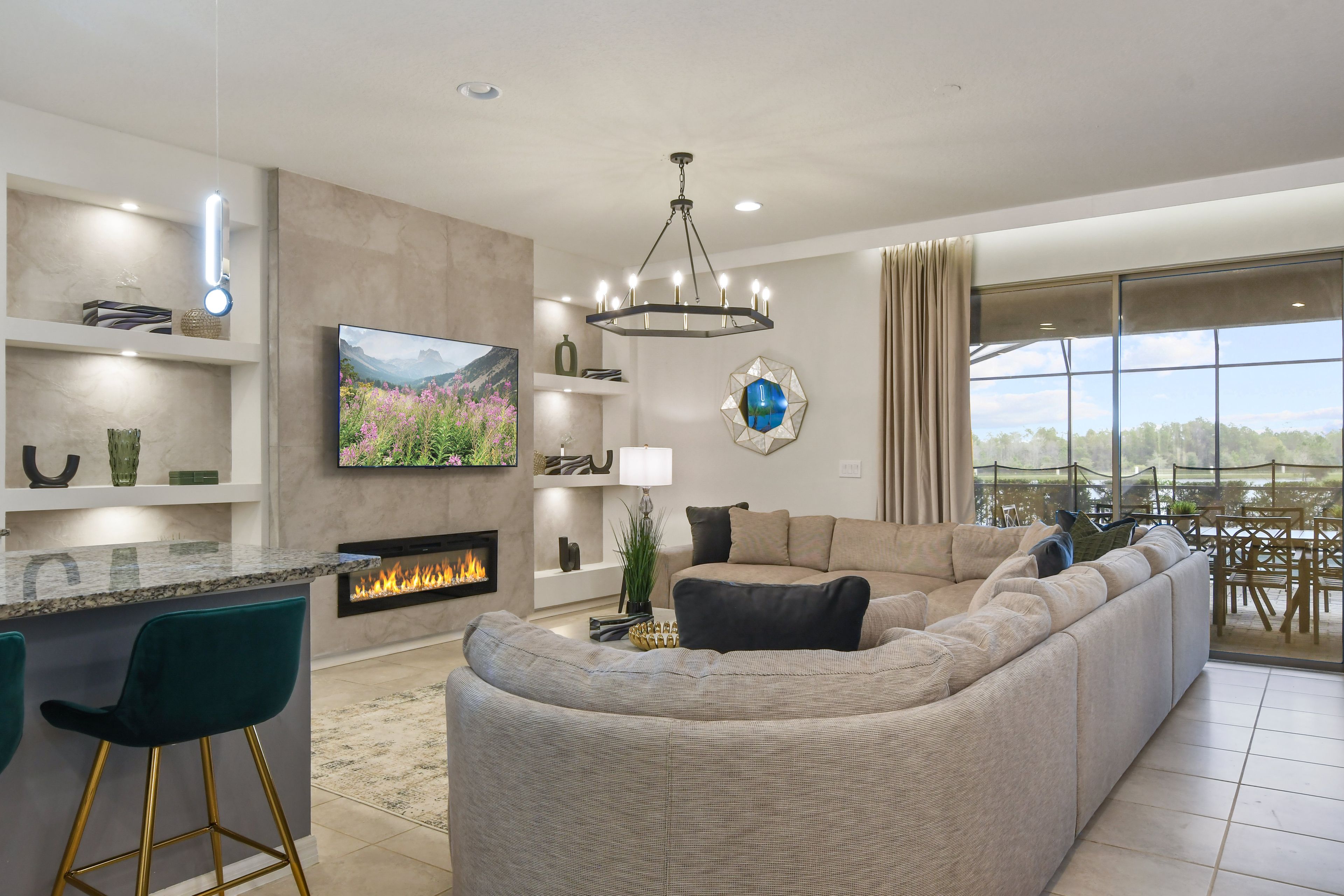 A modern living room with a large L-shaped sectional sofa, a flat-screen TV, a fireplace, and a dining area with a view.