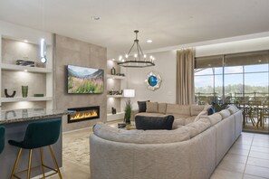 A modern living room with a large L-shaped sectional sofa, a flat-screen TV, a fireplace, and a dining area with a view. - Themed Luxury Villa With Star Wars & Mario Magic (Kissimmee)
