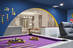 Ein Billardtisch mit Kugeln und Spielstöcken, ein Sofa und eine Mario-Figur in einem Raum mit blauen Wänden und einem gelben Bogen.