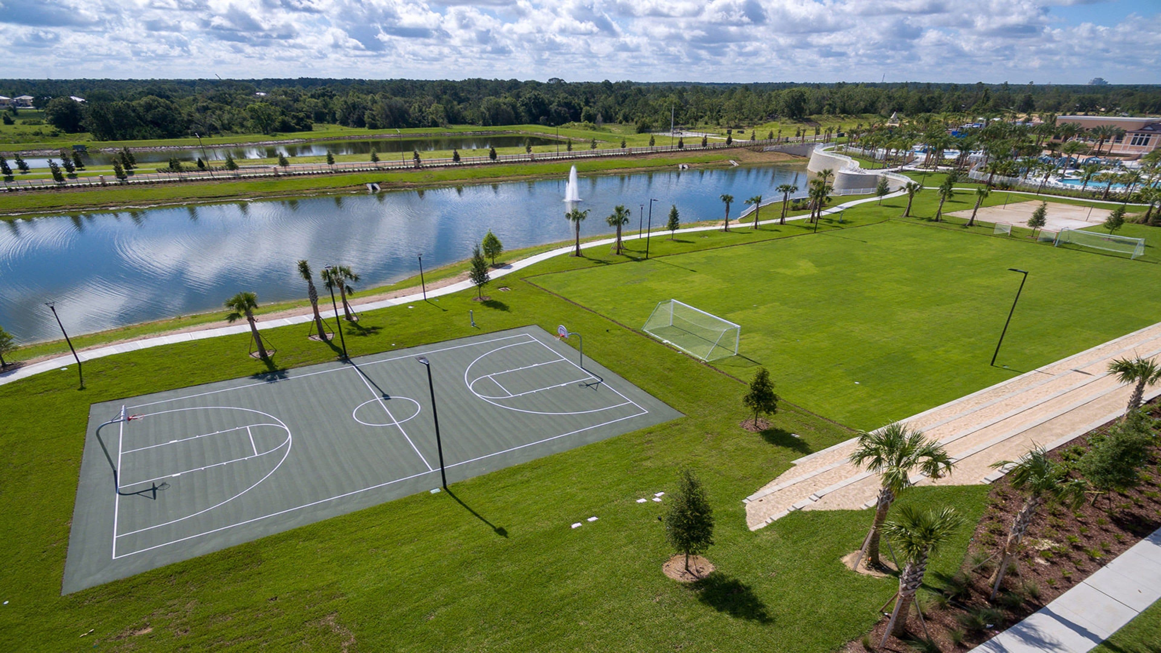 An outdoor basketball court with a water body and trees in the background.