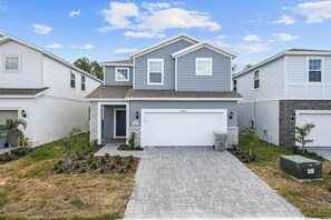 A modern two-story house with a garage, a brick driveway, and small landscaping. - 6BR Villa w/ Private Pool Near Disney (Davenport)